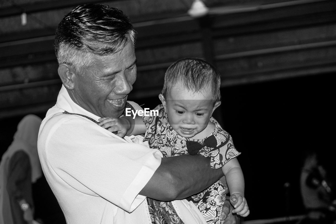 Close-up of happy grandfather carrying crying granddaughter