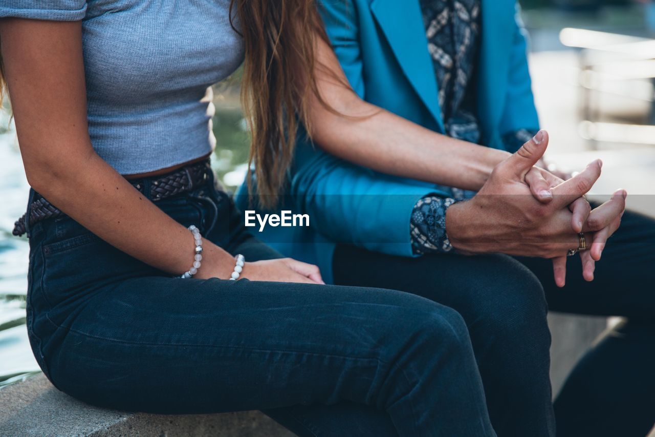 Midsection of couple holding hands while sitting on railing