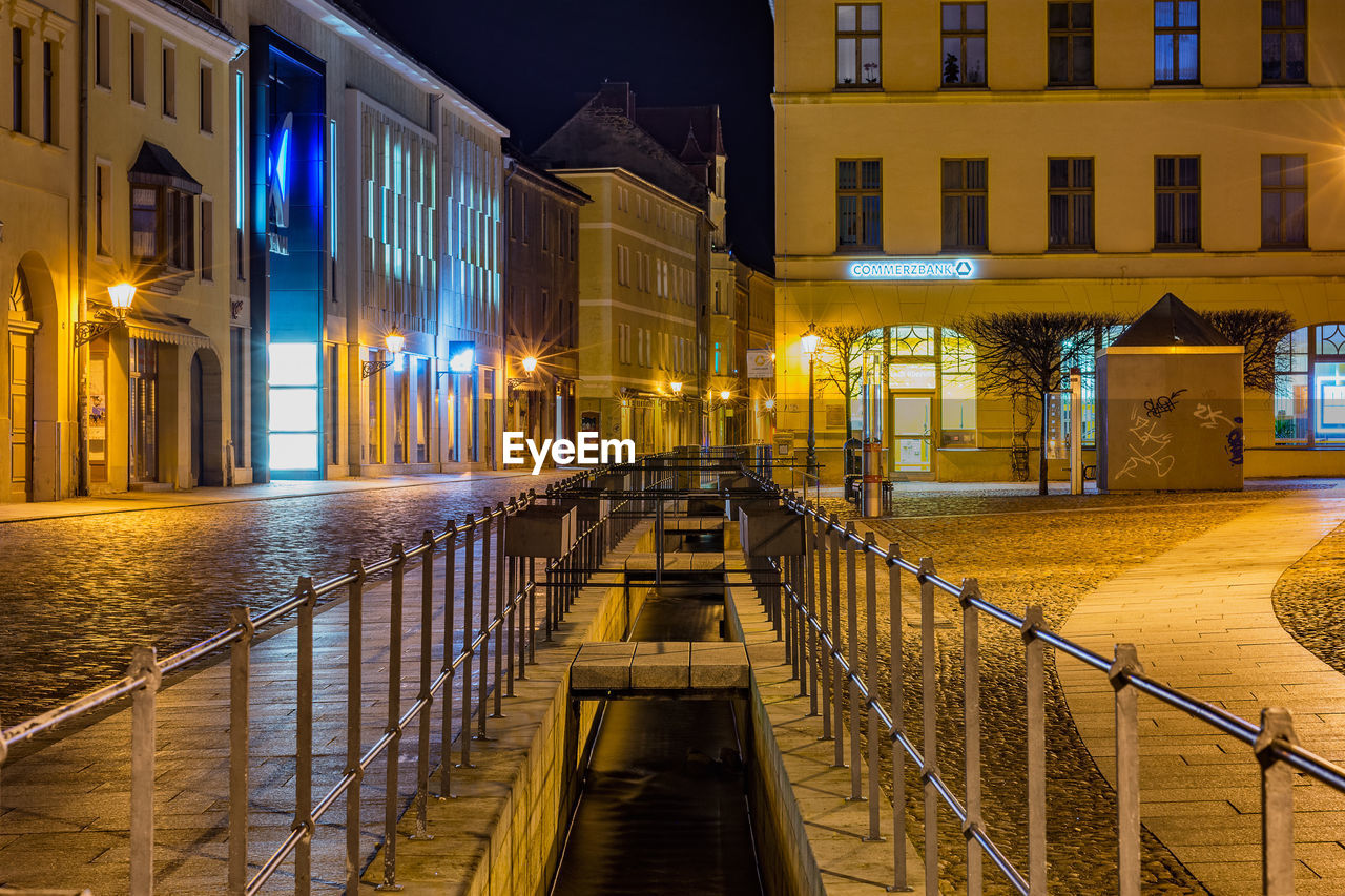 ILLUMINATED FOOTPATH BY BUILDINGS AT NIGHT