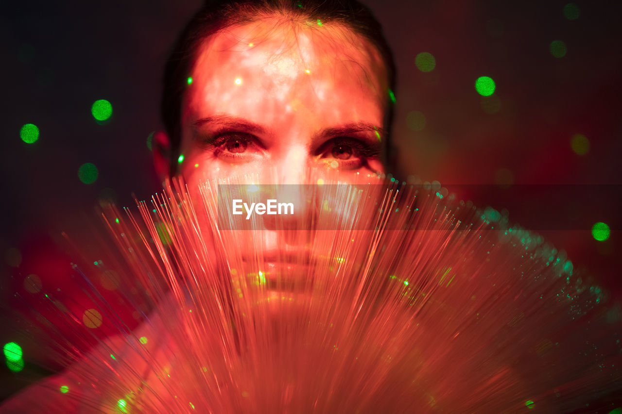 Close-up portrait of young woman against illuminated background