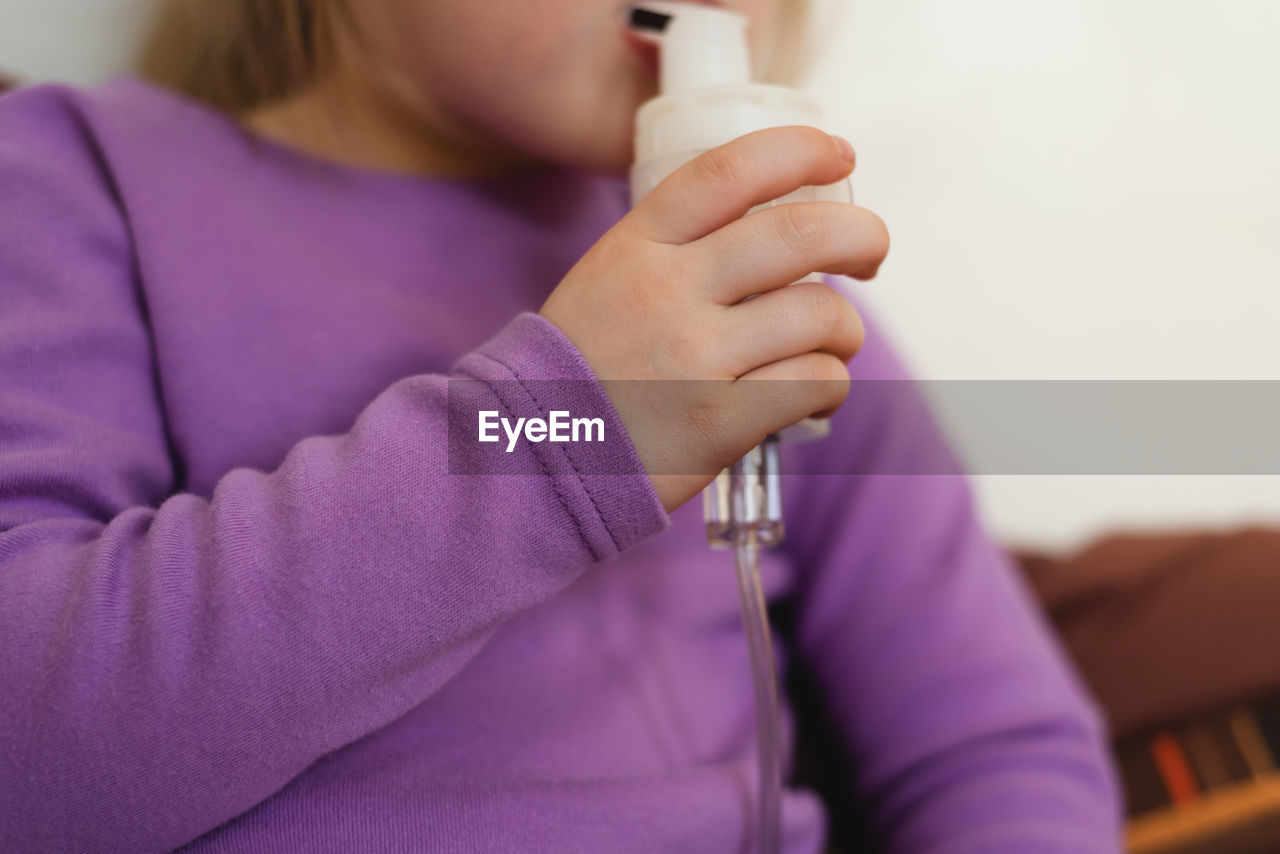 Child lies in bed and makes inhalation using a nebulizer.close-up of a child's hand with a nebulizer