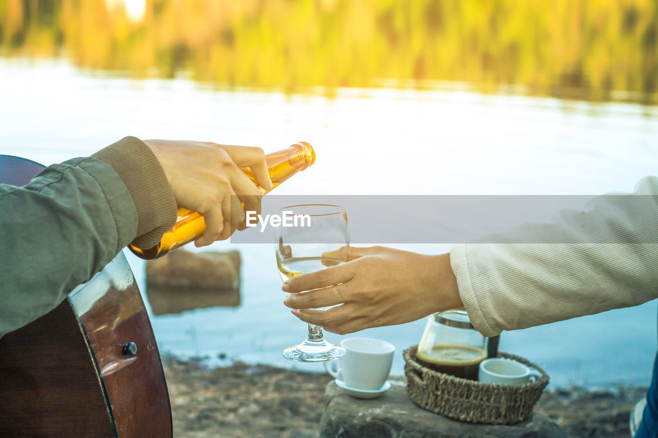 Cropped hand pouring drink for friend by lake