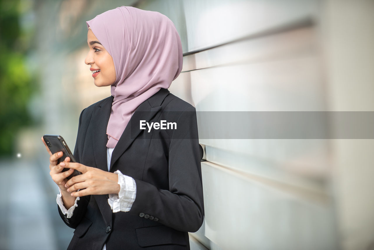 MIDSECTION OF WOMAN HOLDING MOBILE PHONE WHILE STANDING ON LAPTOP