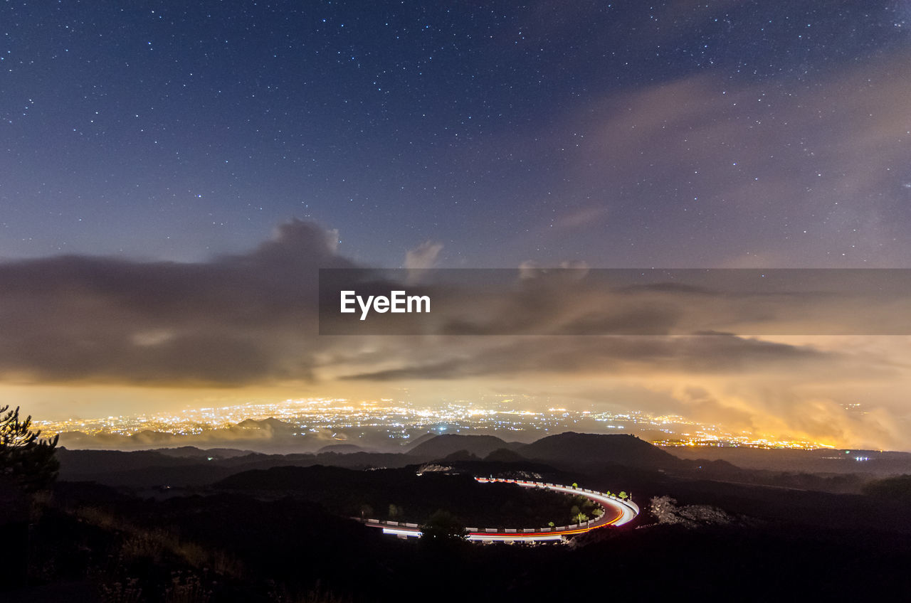 AERIAL VIEW OF ILLUMINATED LIGHT TRAILS AGAINST SKY AT NIGHT