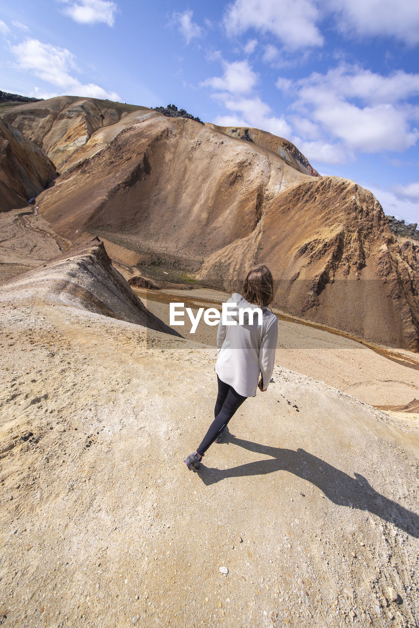 View from top of young woman walking downhill on sand dune