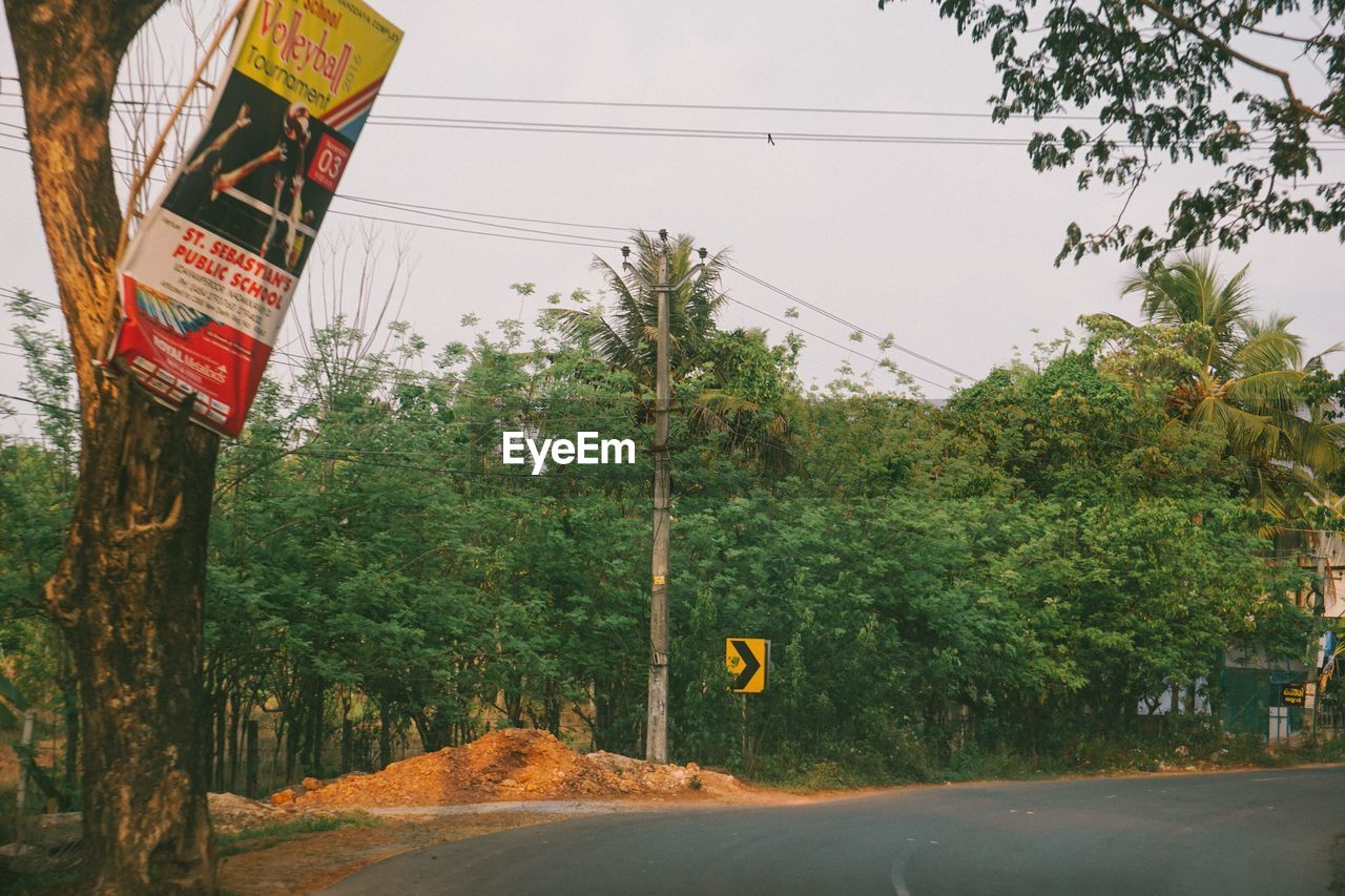 ROAD SIGN BY TREES AGAINST SKY IN BACKGROUND