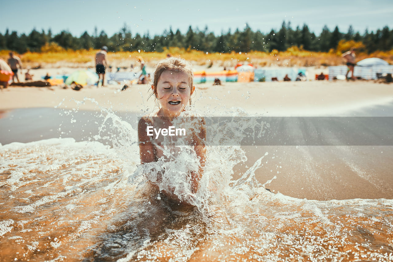 Little girl splashed by sea wave while sitting and playing on a beach. child enjoying the sea