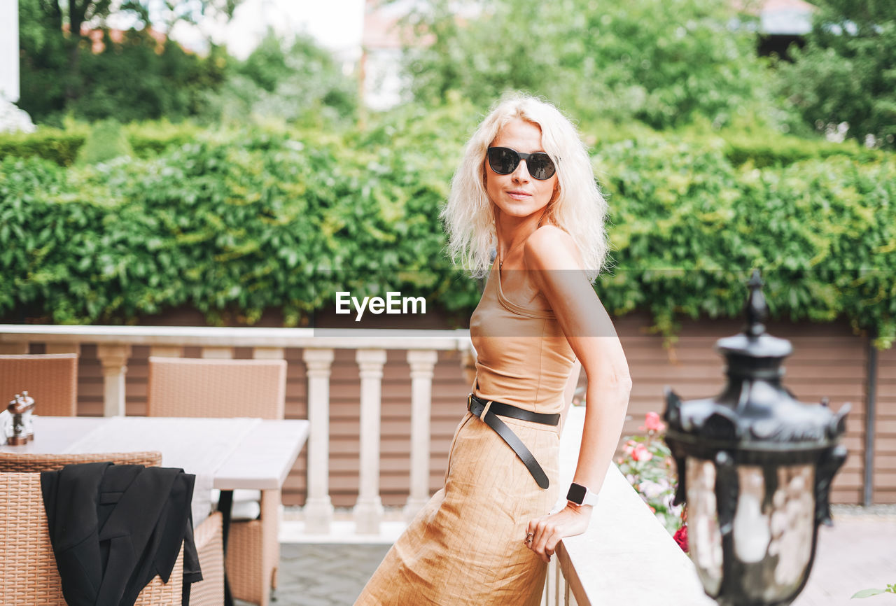 Adult elegant blonde woman in sunglasses beige clothes in summer city street cafe