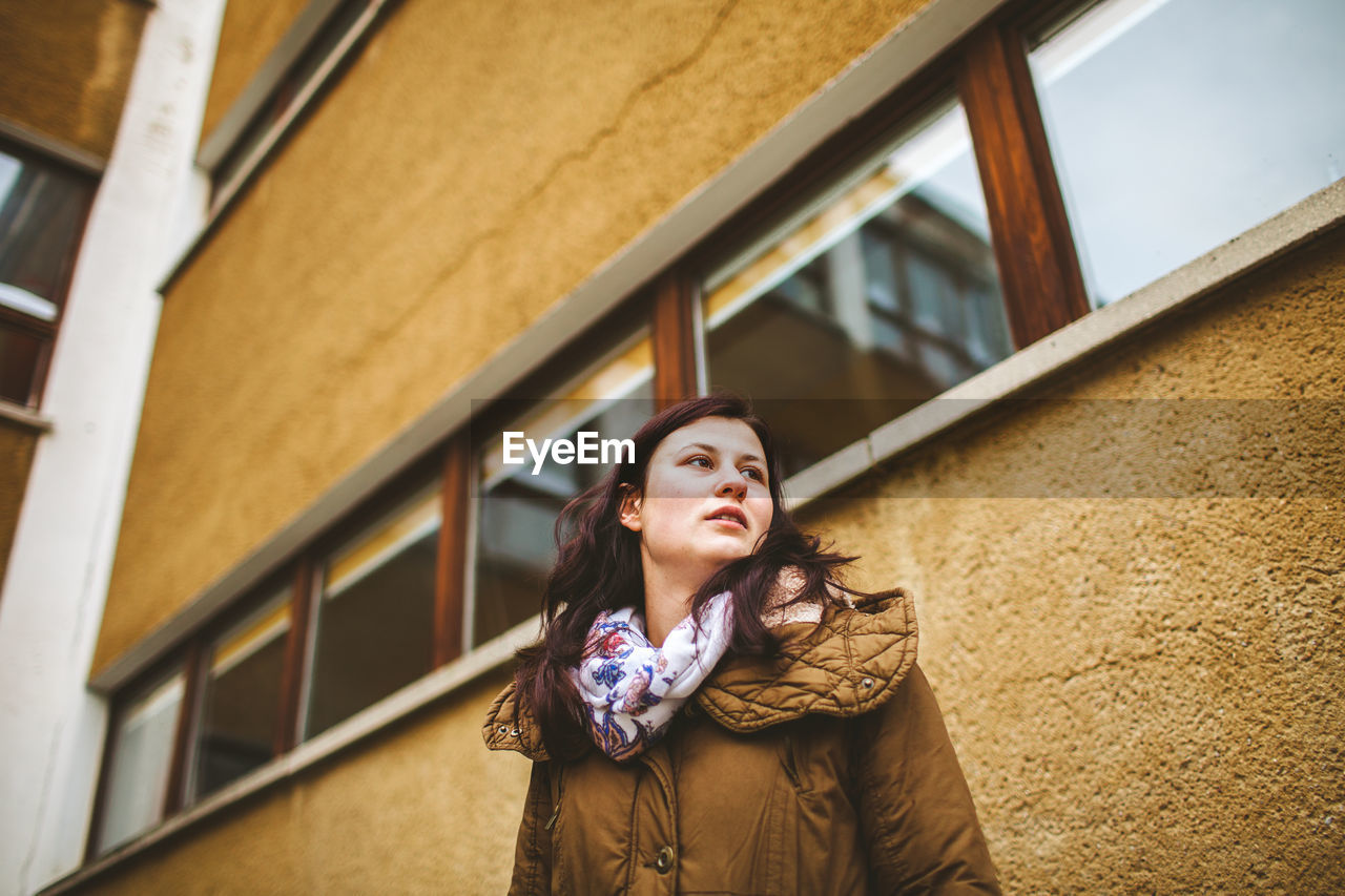 Portrait of young woman looking away while standing against building