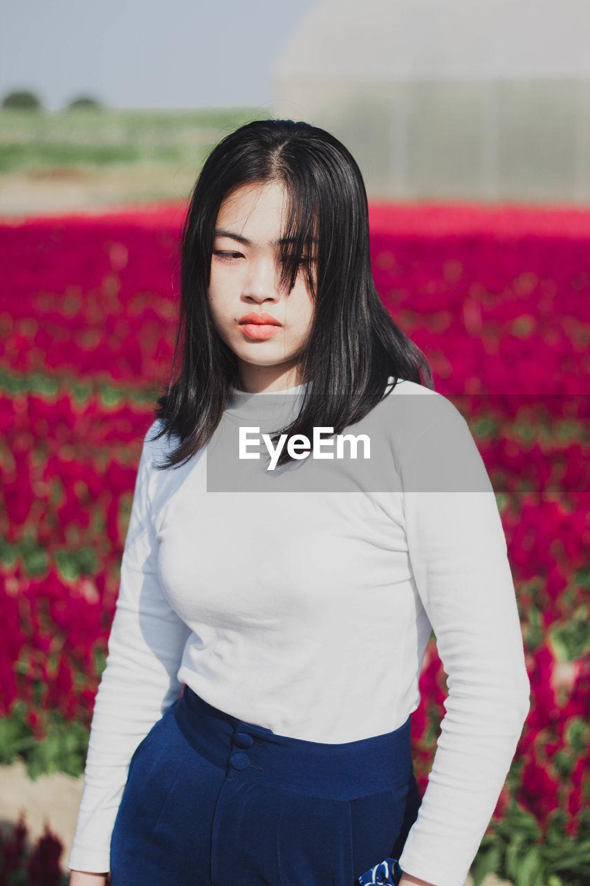 Portrait of beautiful woman standing by red flower