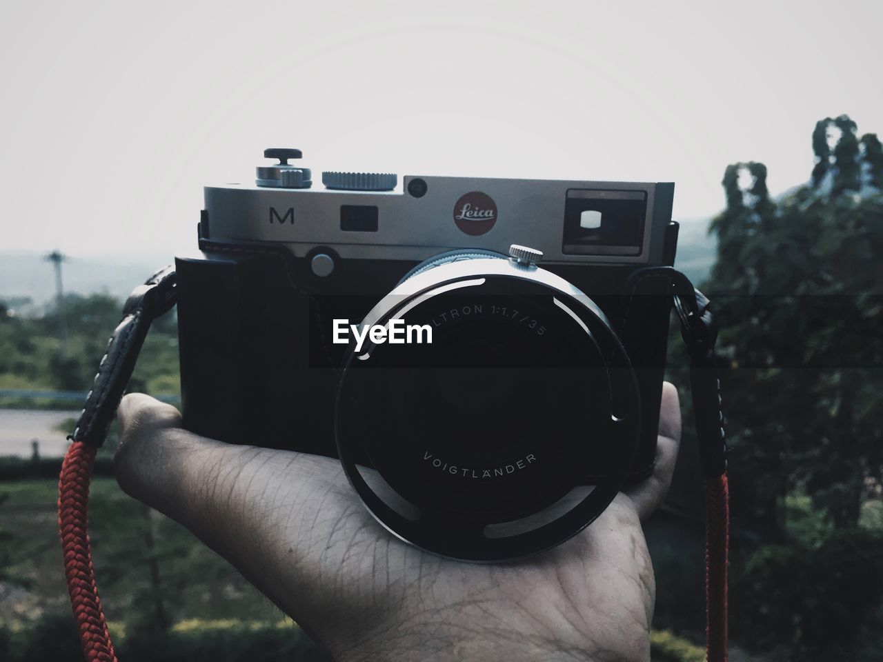 CLOSE-UP OF HAND HOLDING CAMERA WITH SUNGLASSES