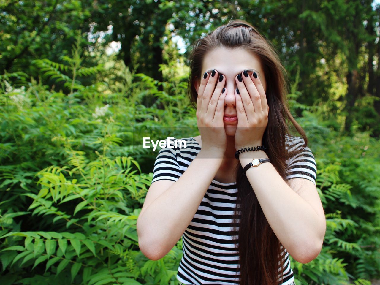 Young woman covering face while standing against plants