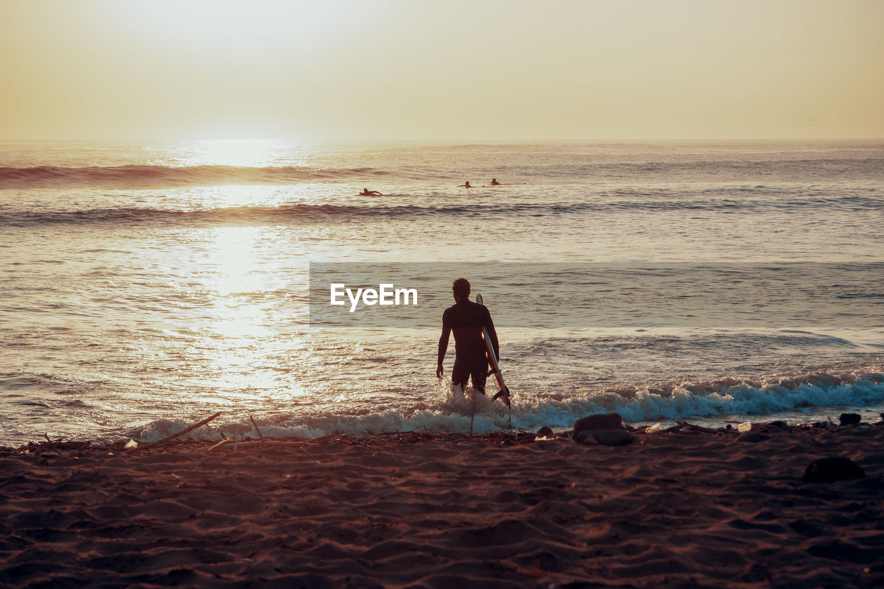 Silhouette male surfer in sea against clear sky during sunset