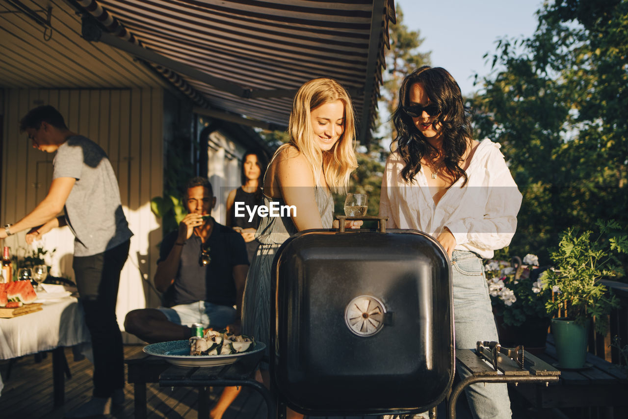 Female friends talking while grilling food on barbecue in dinner party