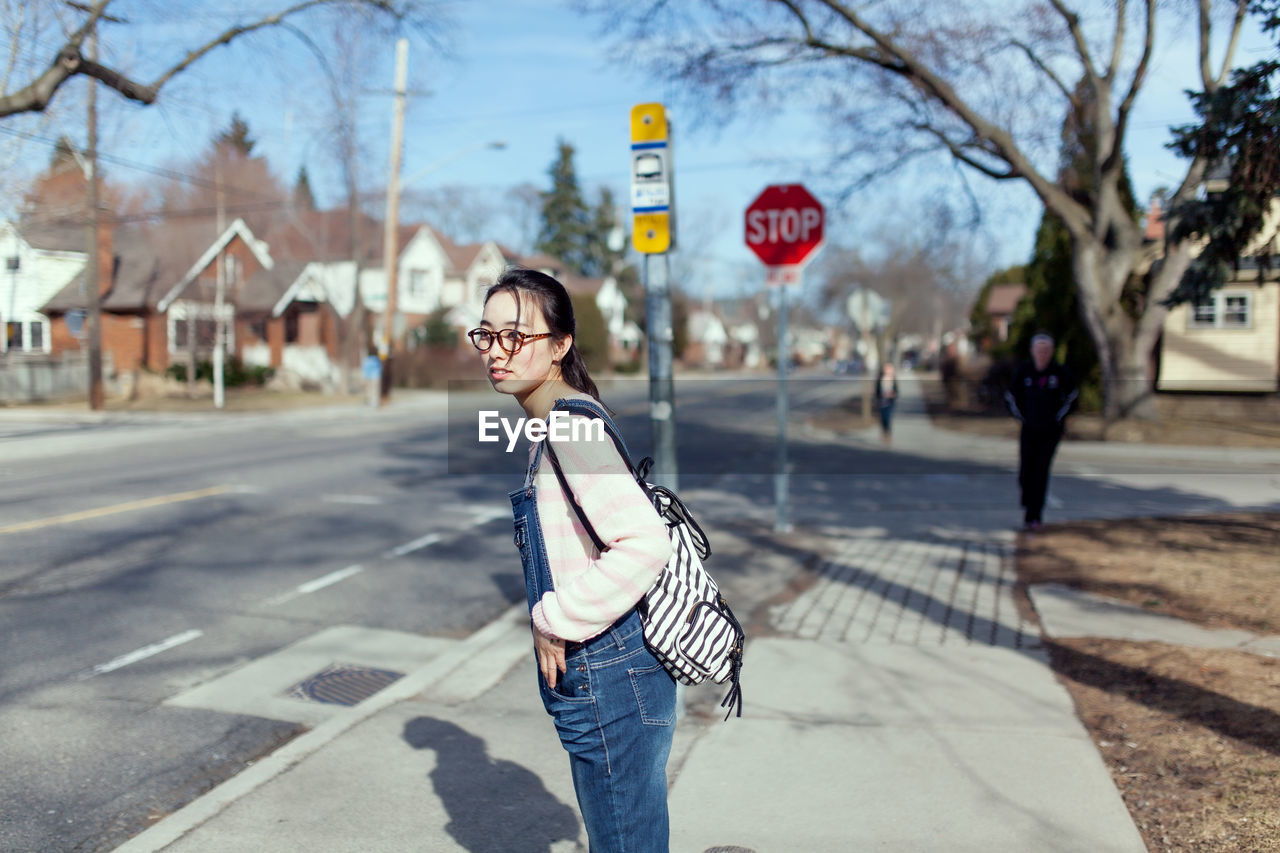 Side view of woman with backpack looking away while standing on sidewalk