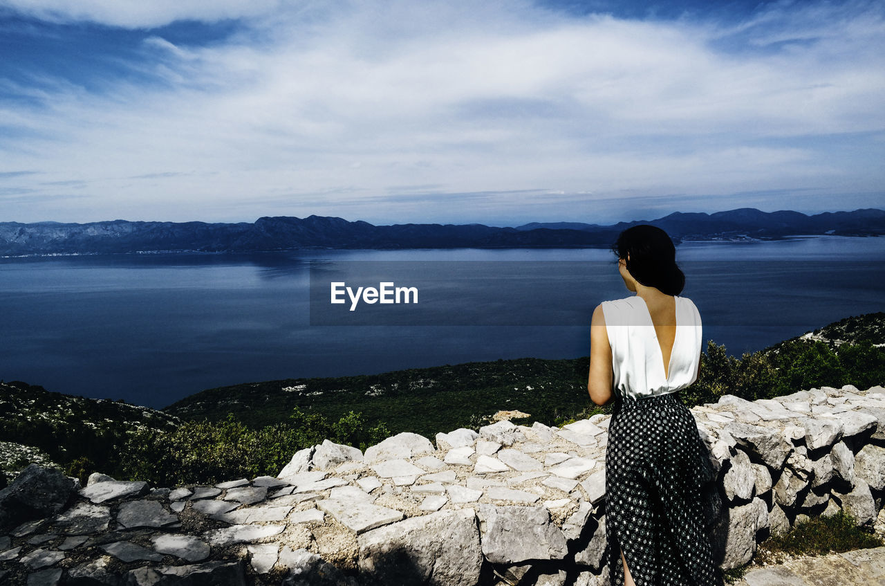 Rear view of woman standing by lake against cloudy sky