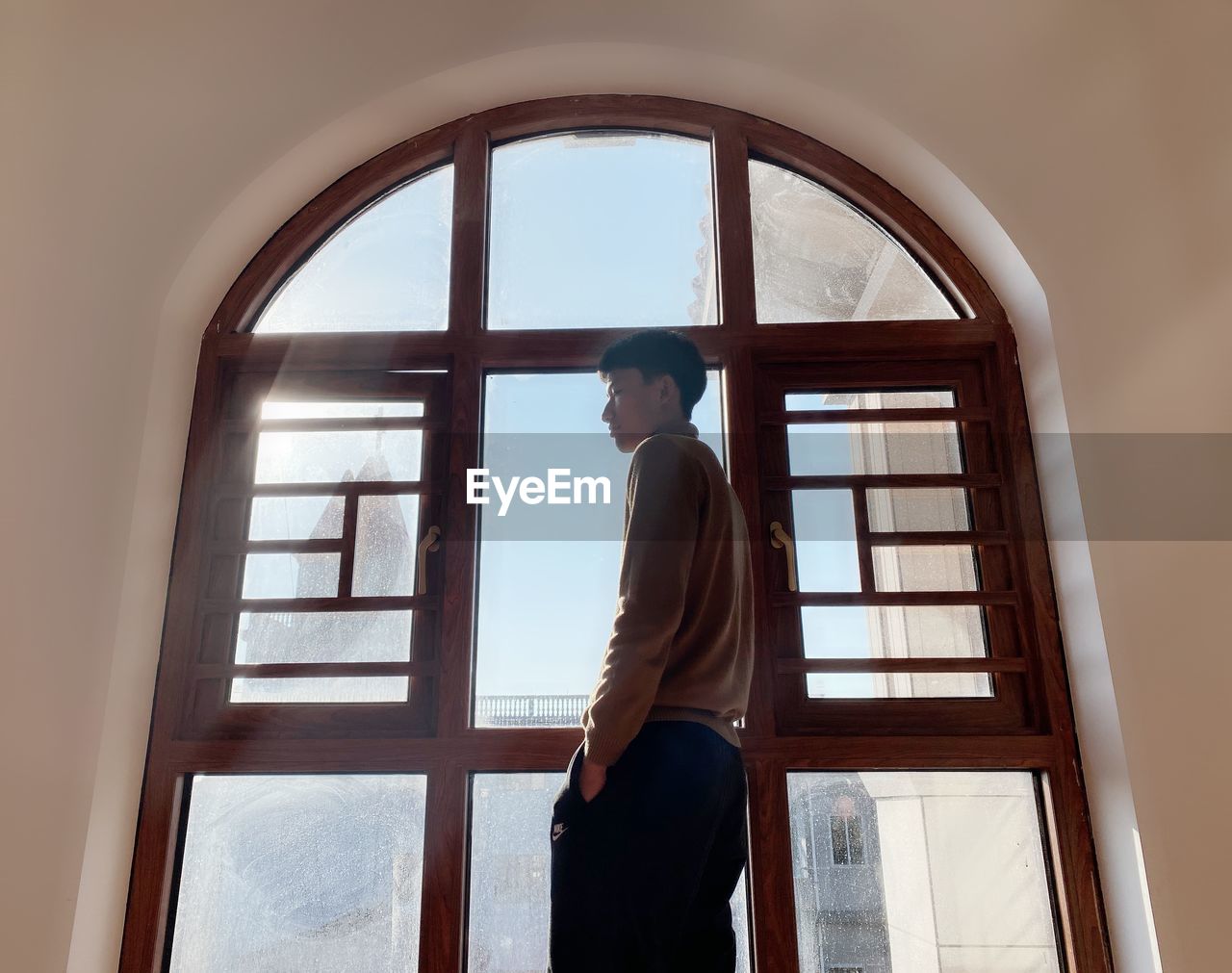 FULL LENGTH OF YOUNG MAN STANDING BY WINDOW AT HOME