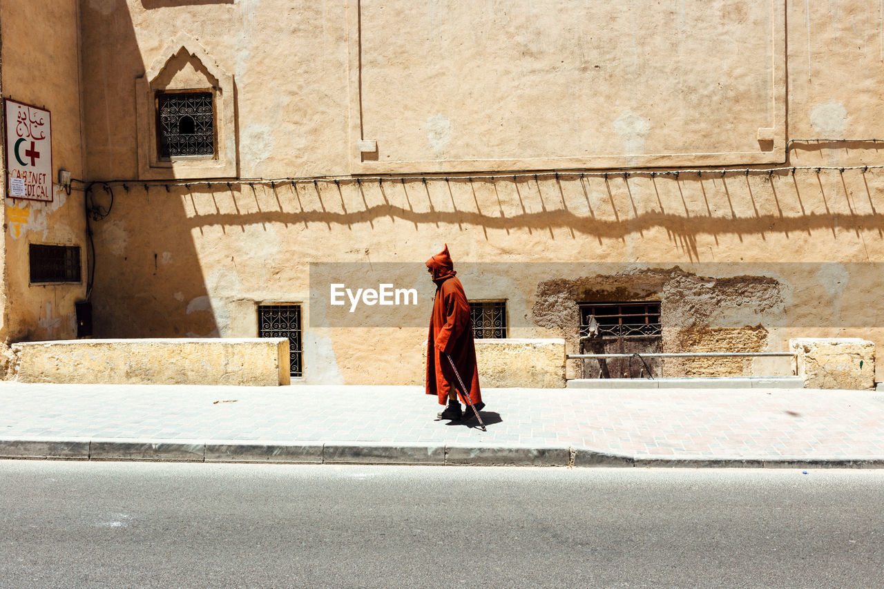 Side view of man walking on footpath by building in city