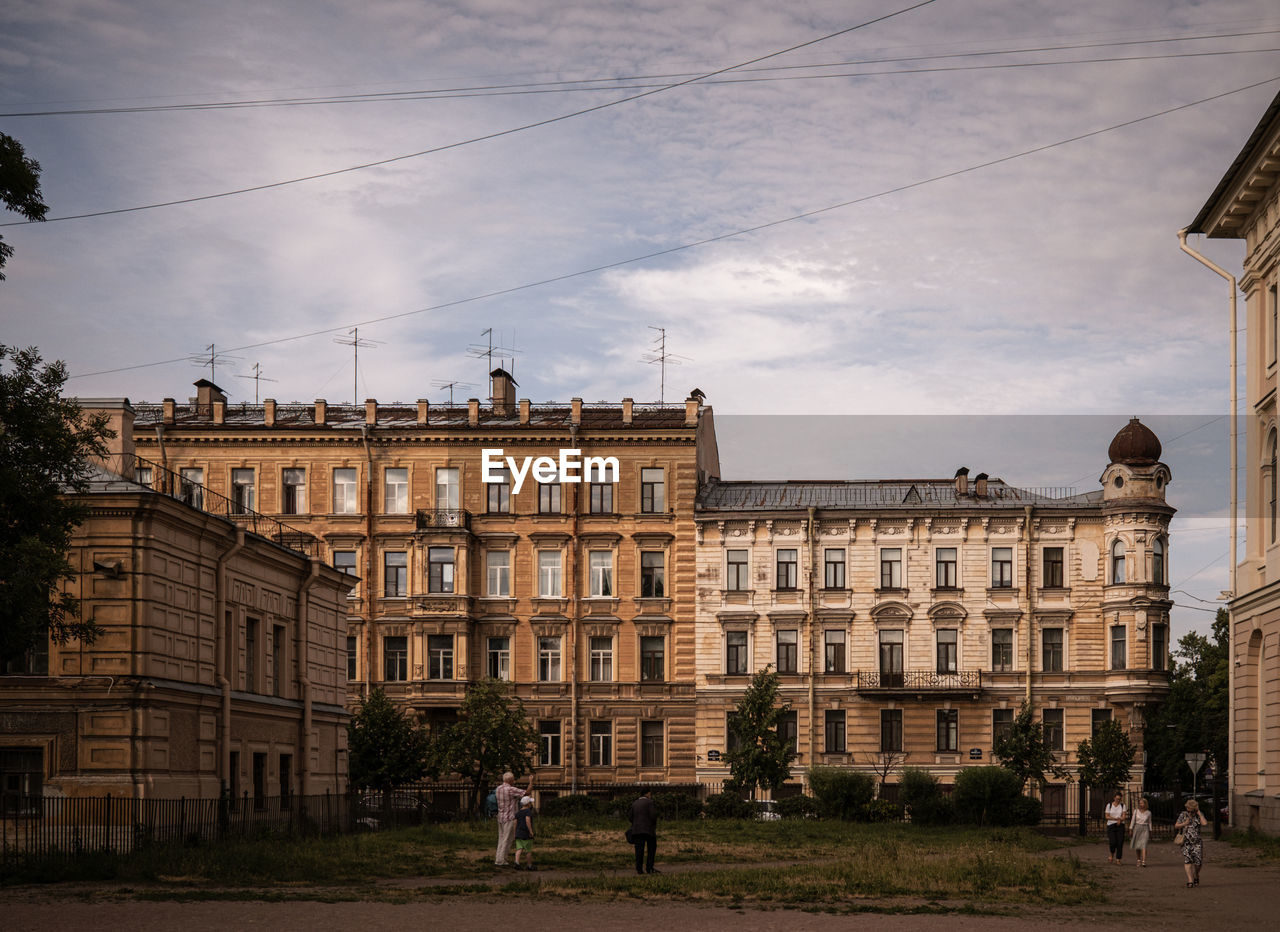 People walking by old buildings in city against sky