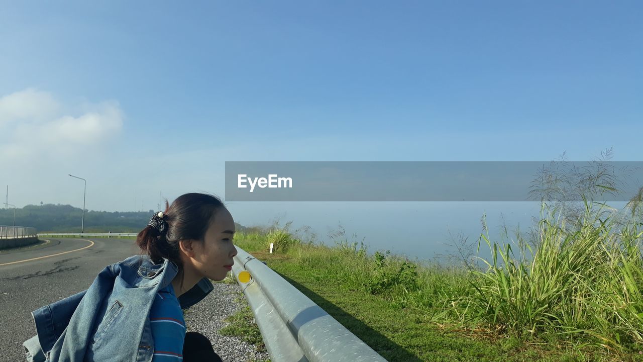 Woman smiling on road amidst field against sky