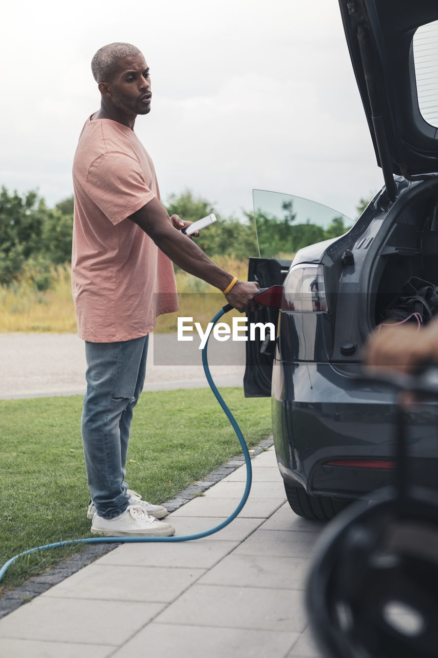 Full length side view of man charging electric car at station