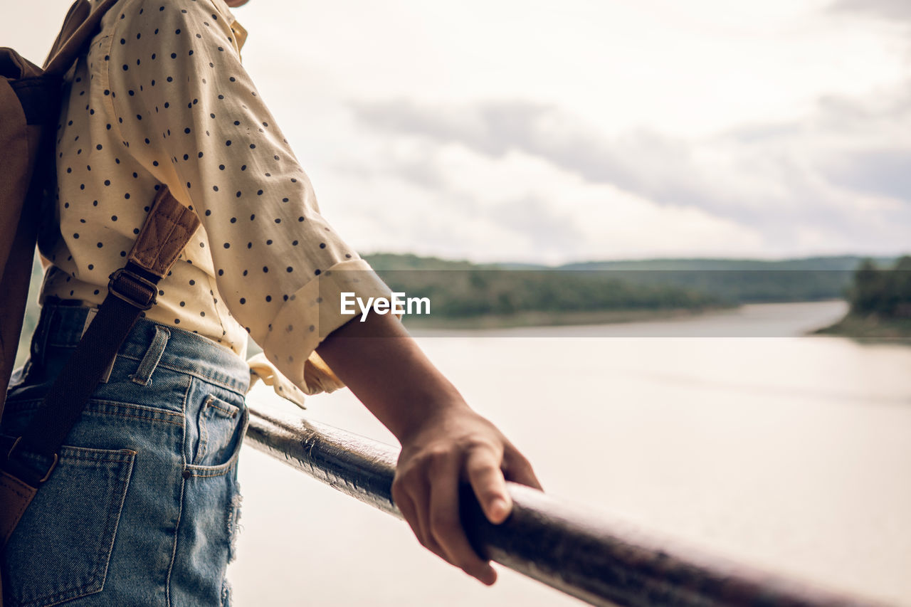 WOMAN STANDING ON RAILING AGAINST SKY