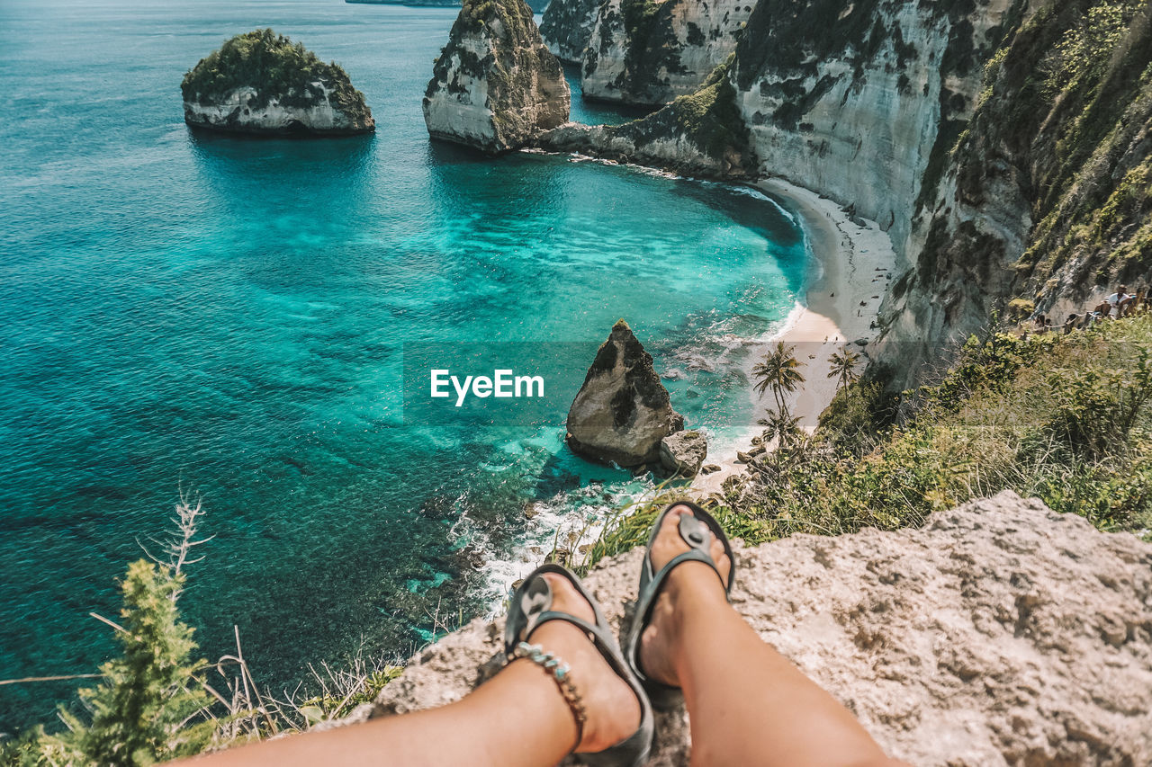 Low section of woman sitting on cliff over sea