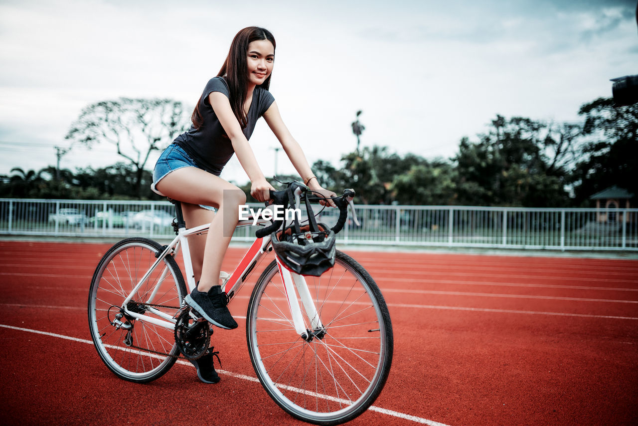 SIDE VIEW OF YOUNG WOMAN WITH BICYCLE ON SKATEBOARD