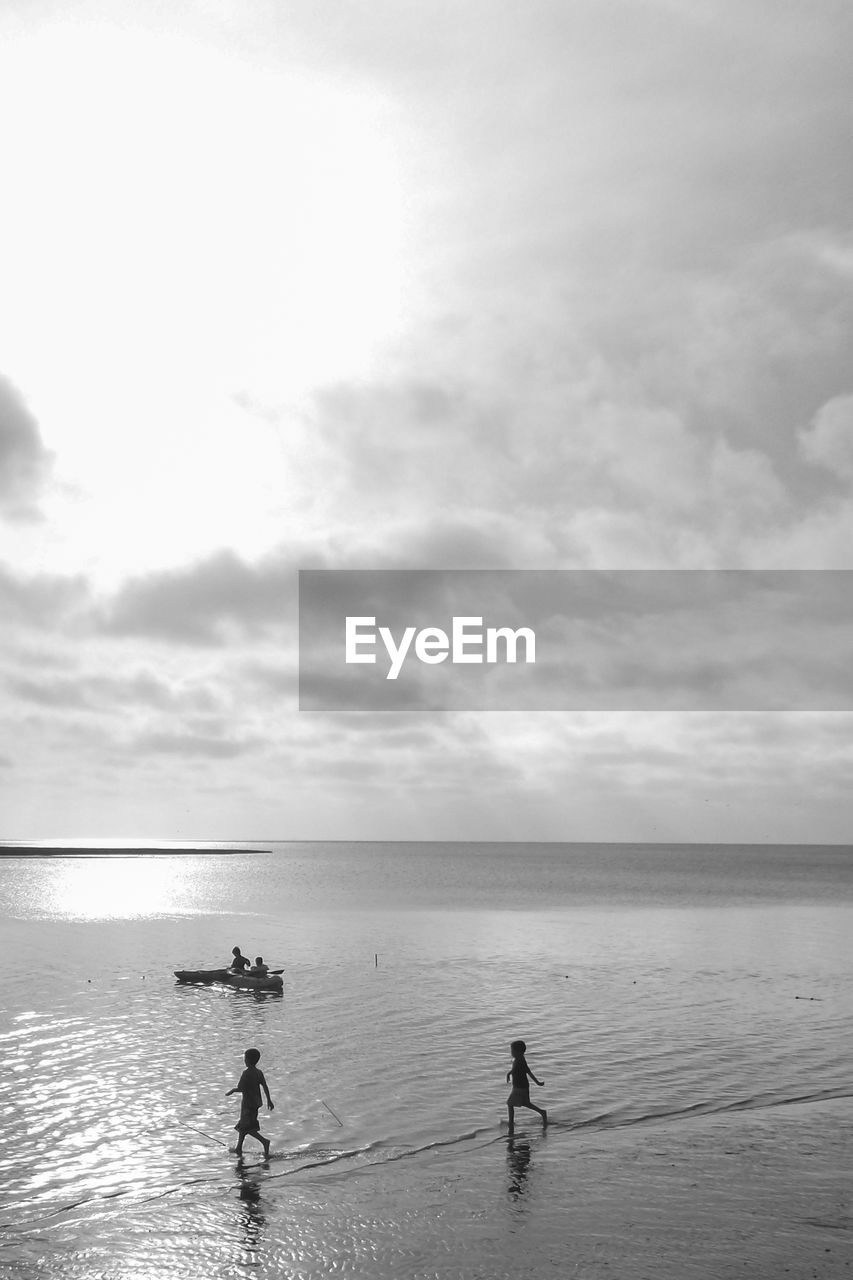 PEOPLE STANDING AT BEACH AGAINST SKY