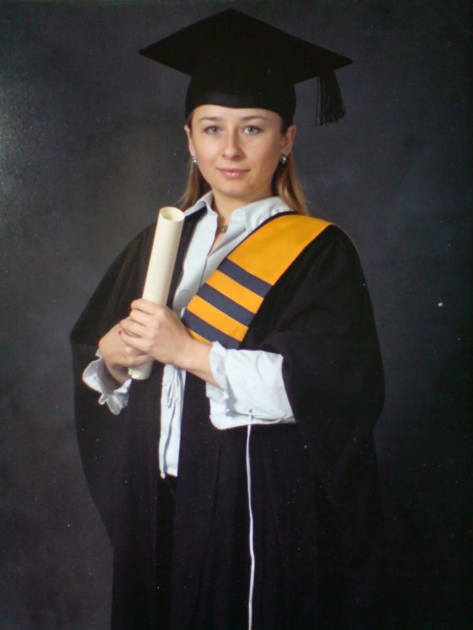 Portrait of woman in graduation gown holding diploma against black background