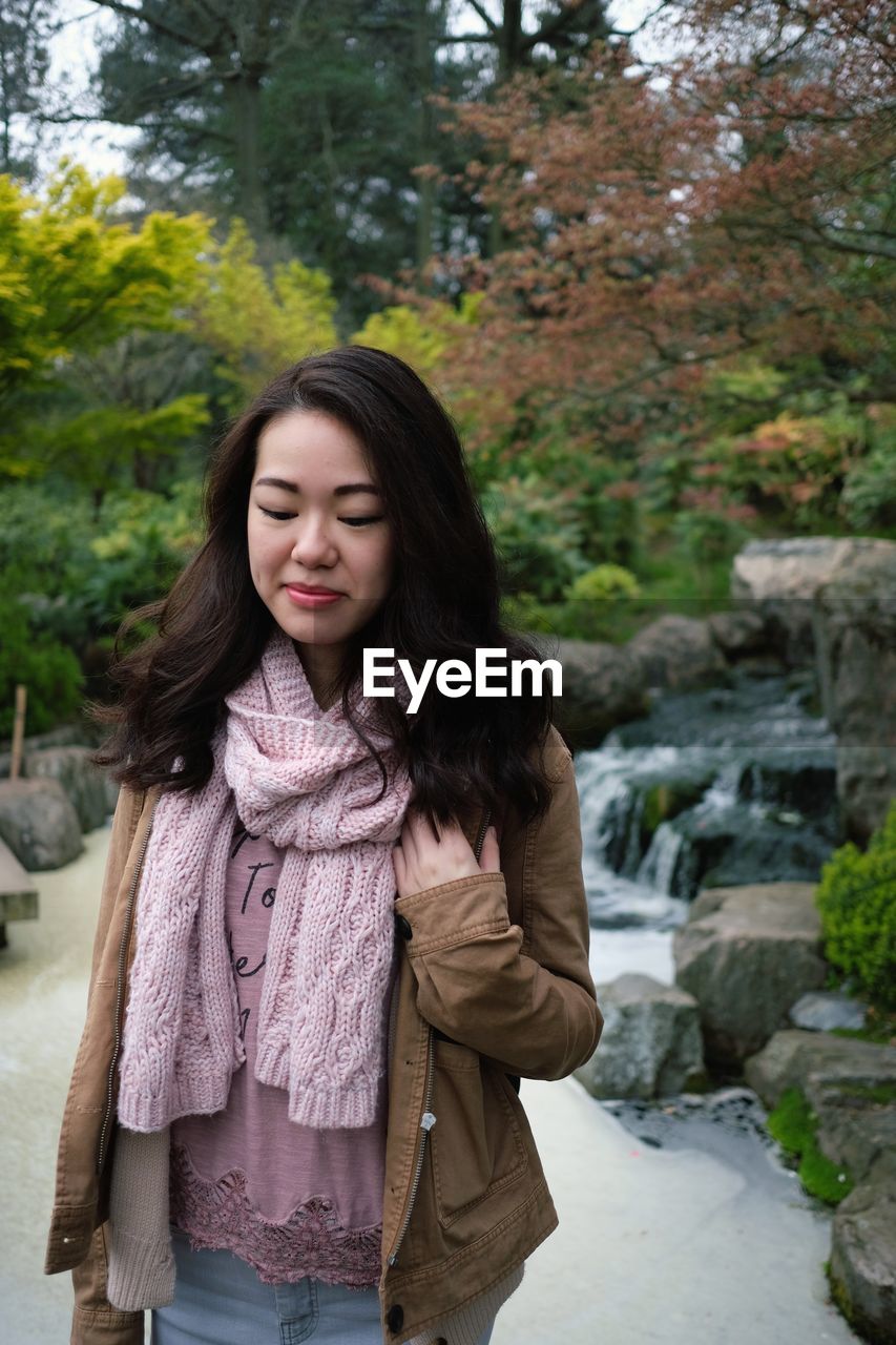 Young woman looking away while standing against trees