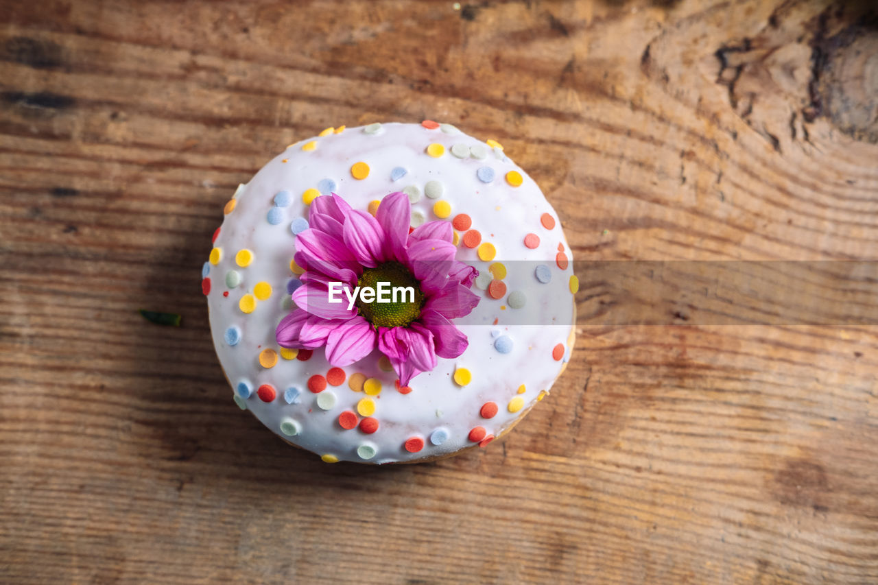 Chamomile bud on top of donut on wooden background. delicate frame with pink flower