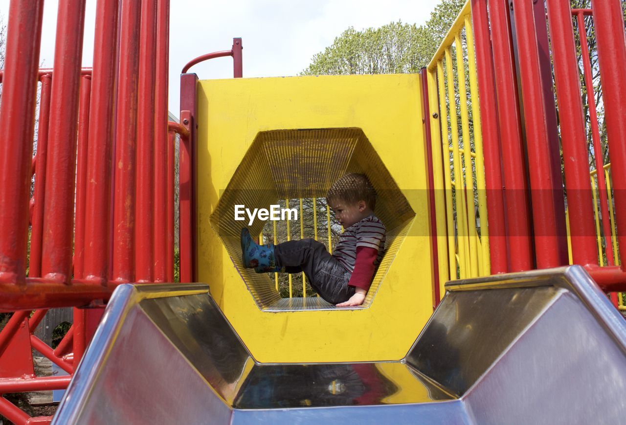 Side view full length of playful boy in play equipment at park