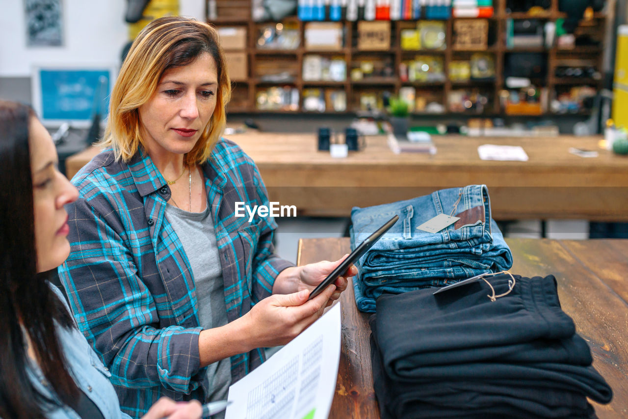 Portrait of blonde young woman holding digital tablet while checking clothes stock on local store