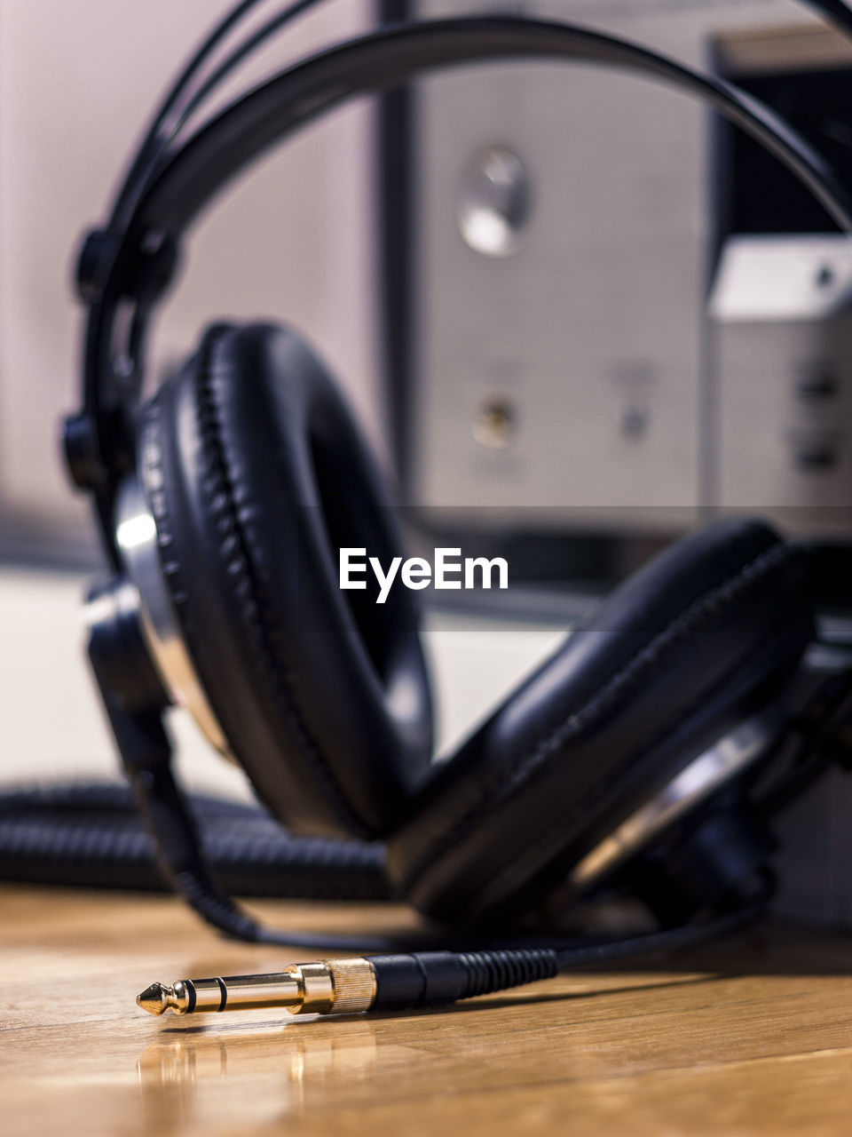 Black hi-fi headphones with a gold input jack on a wooden floor