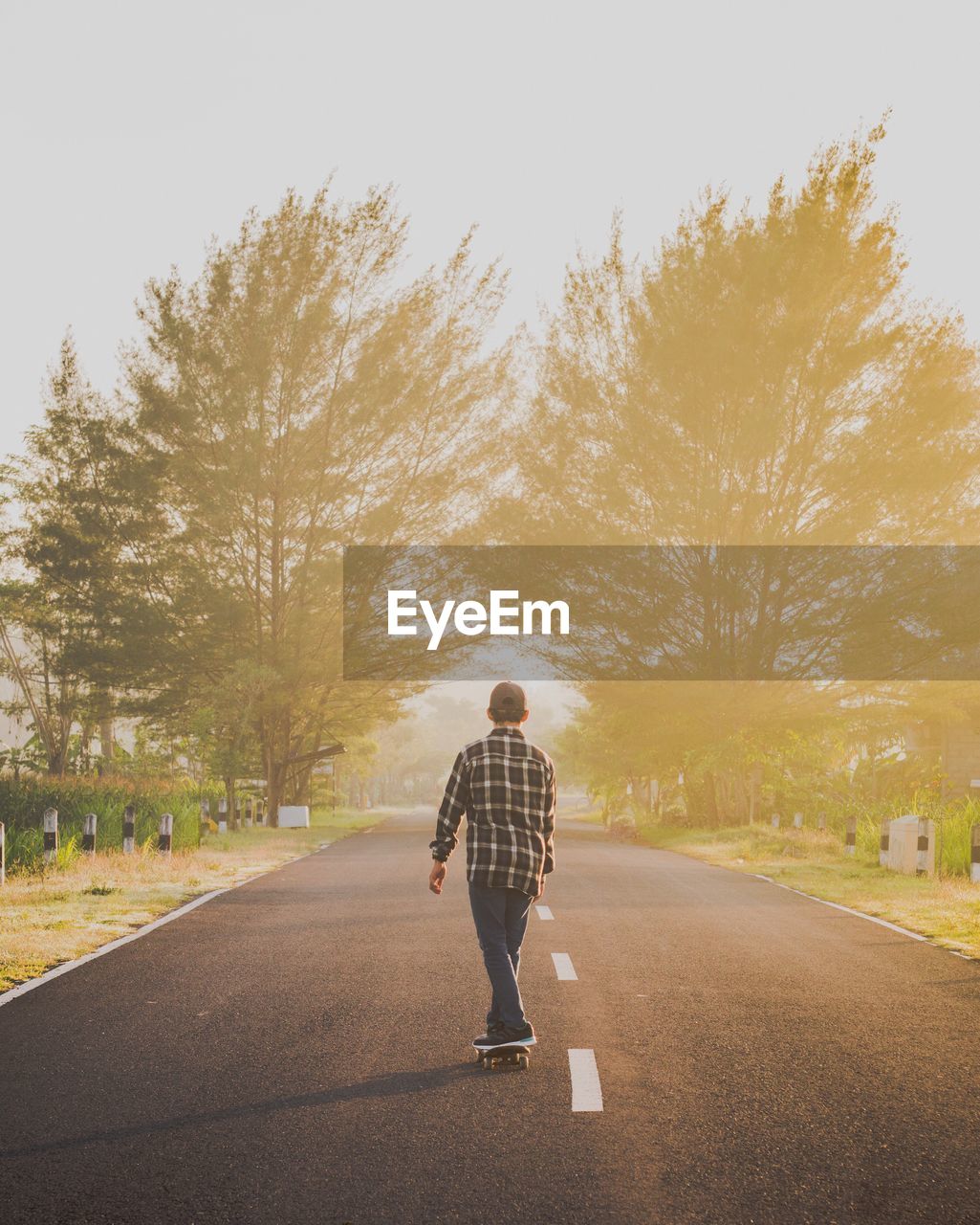 Rear angle view of young boy skateboarding on country road at sunset