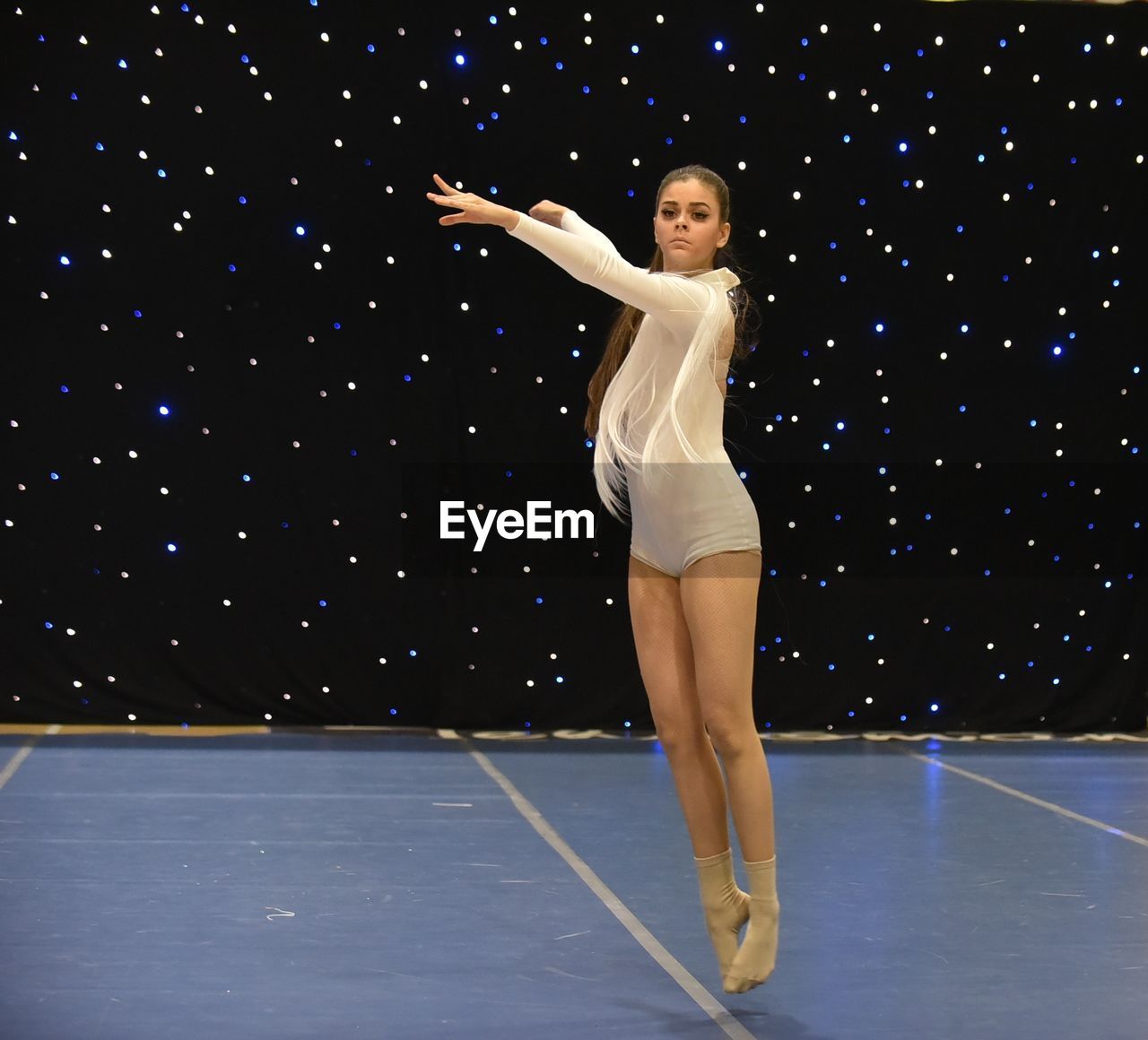 Young teenage girl dances on stage in a white leotard