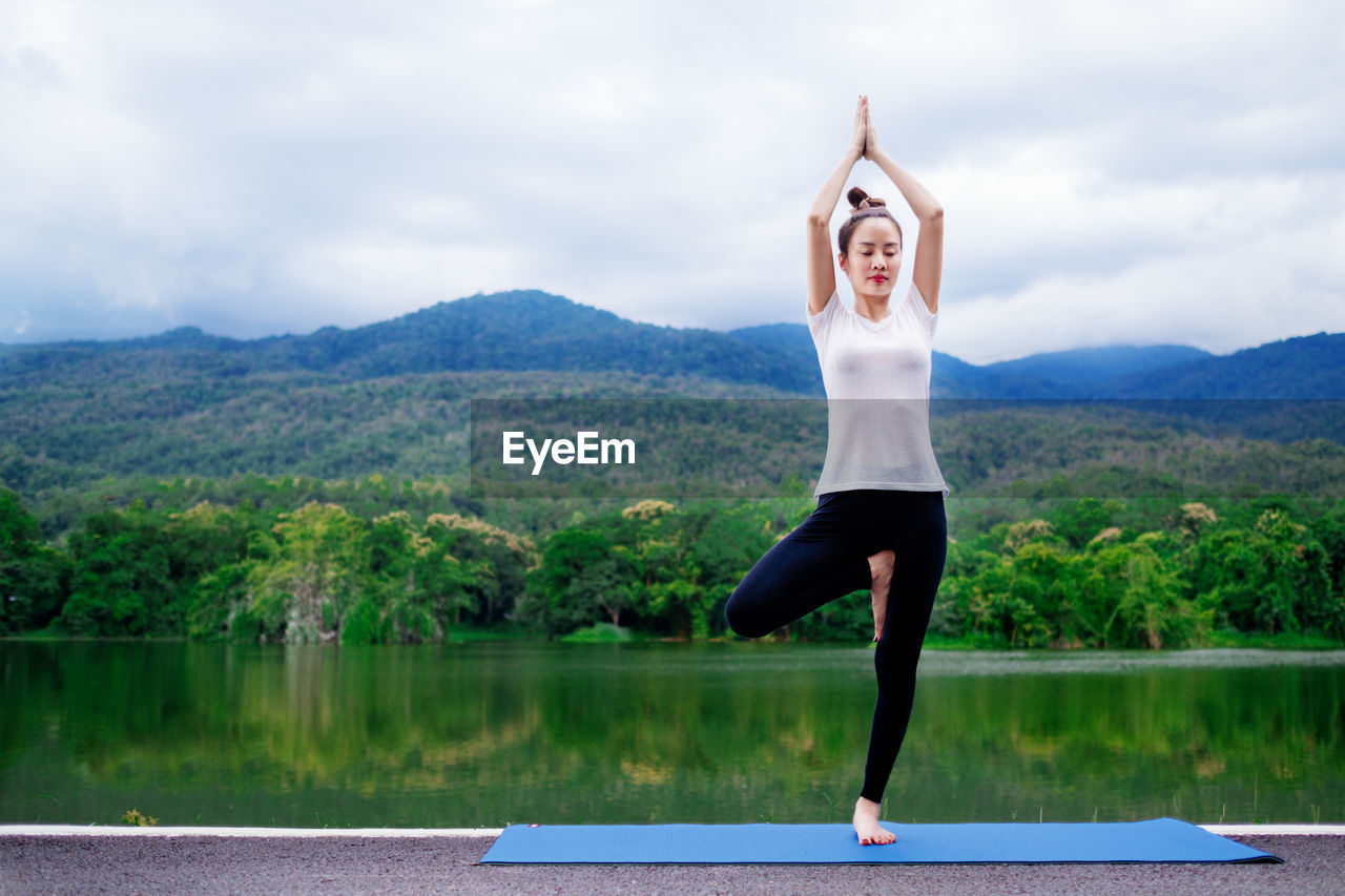 Full length of woman doing yoga against lake