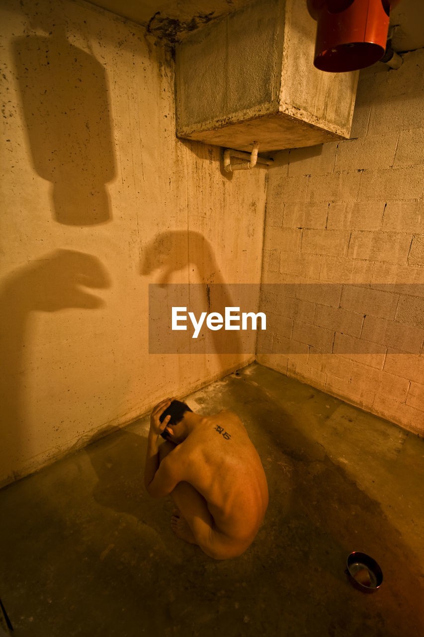 High angle view of naked man sitting in abandoned bathroom