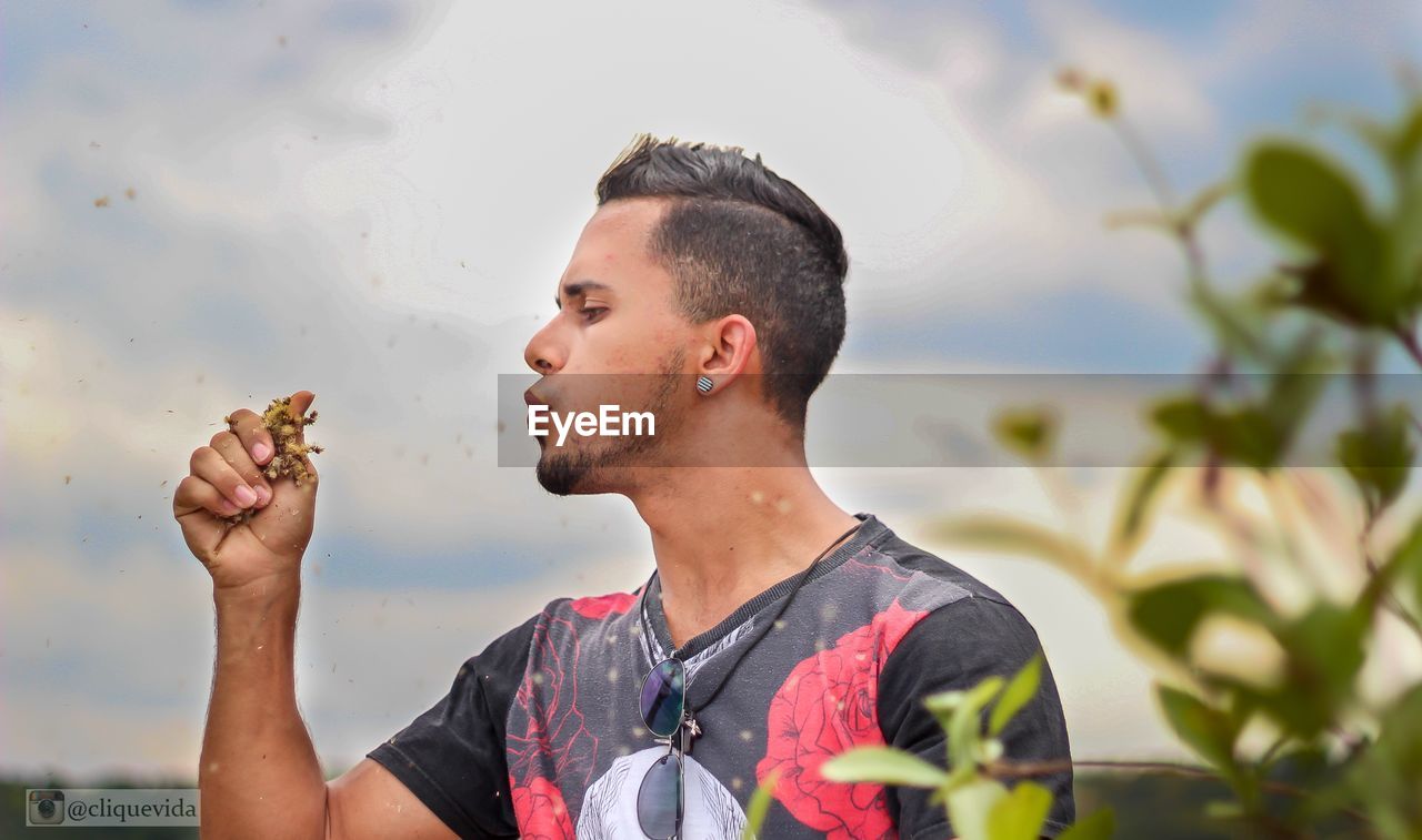 Young man blowing dry plants against sky