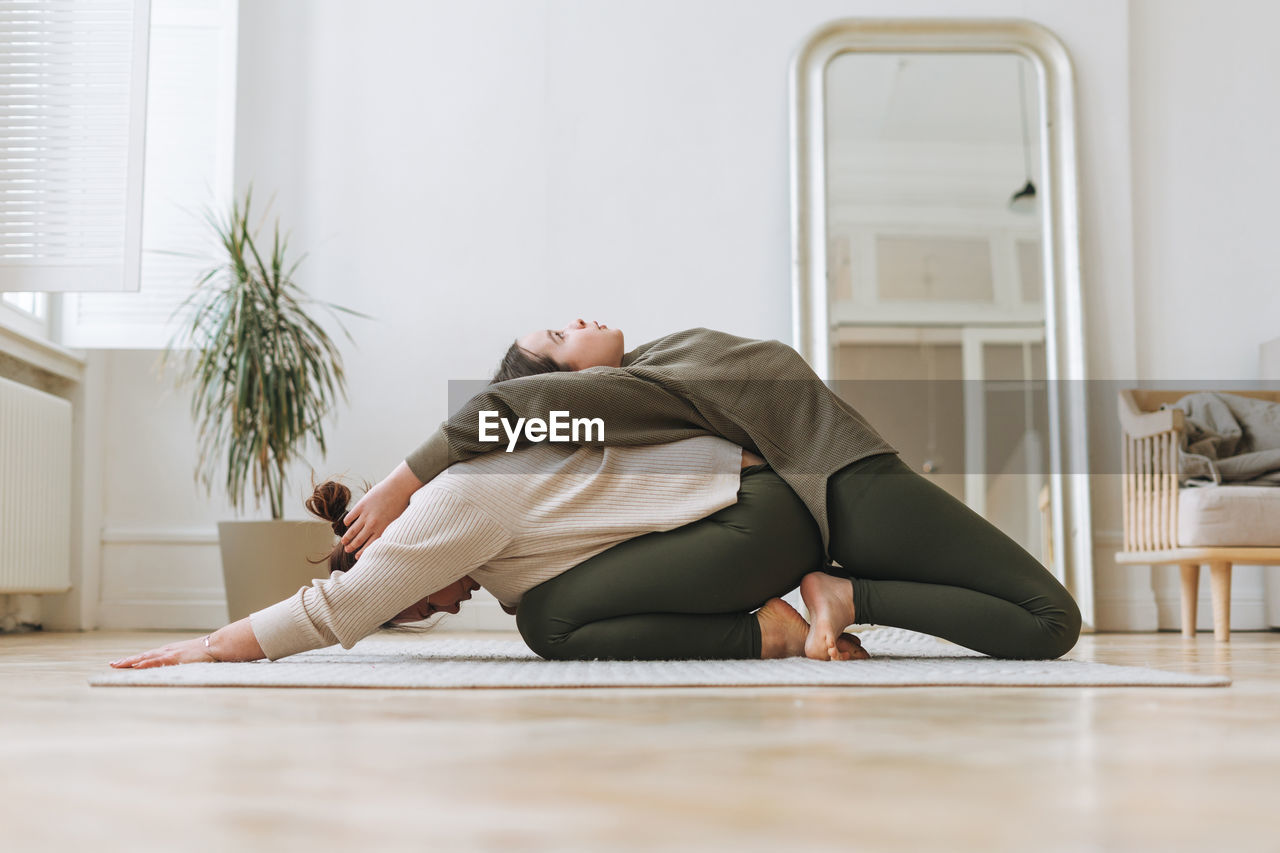 Attractive mother middle age woman and daughter teenager ptactice yoga together in the bright room