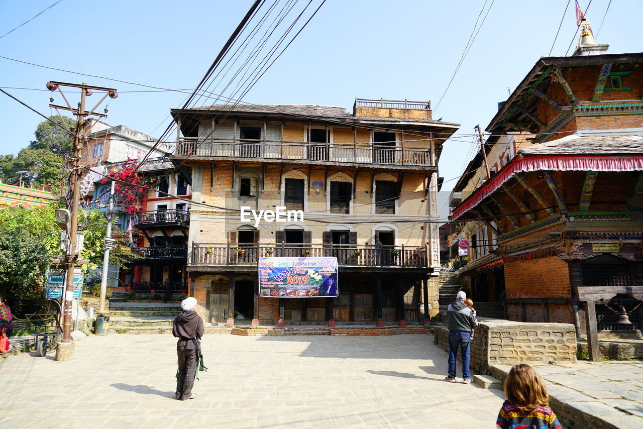 REAR VIEW OF PEOPLE WALKING ON STREET AGAINST BUILDINGS