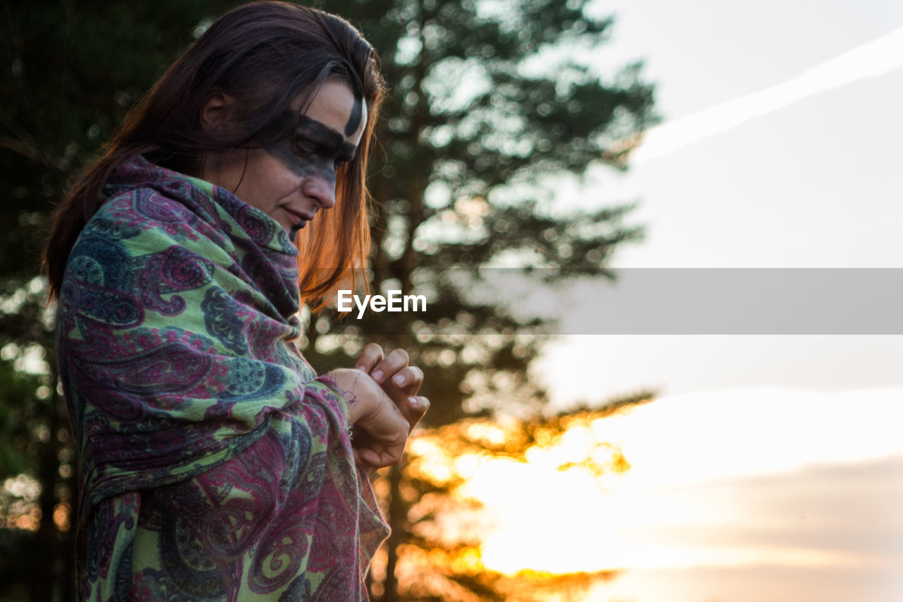 Side view of woman with black face paint wrapped in blanket during sunset
