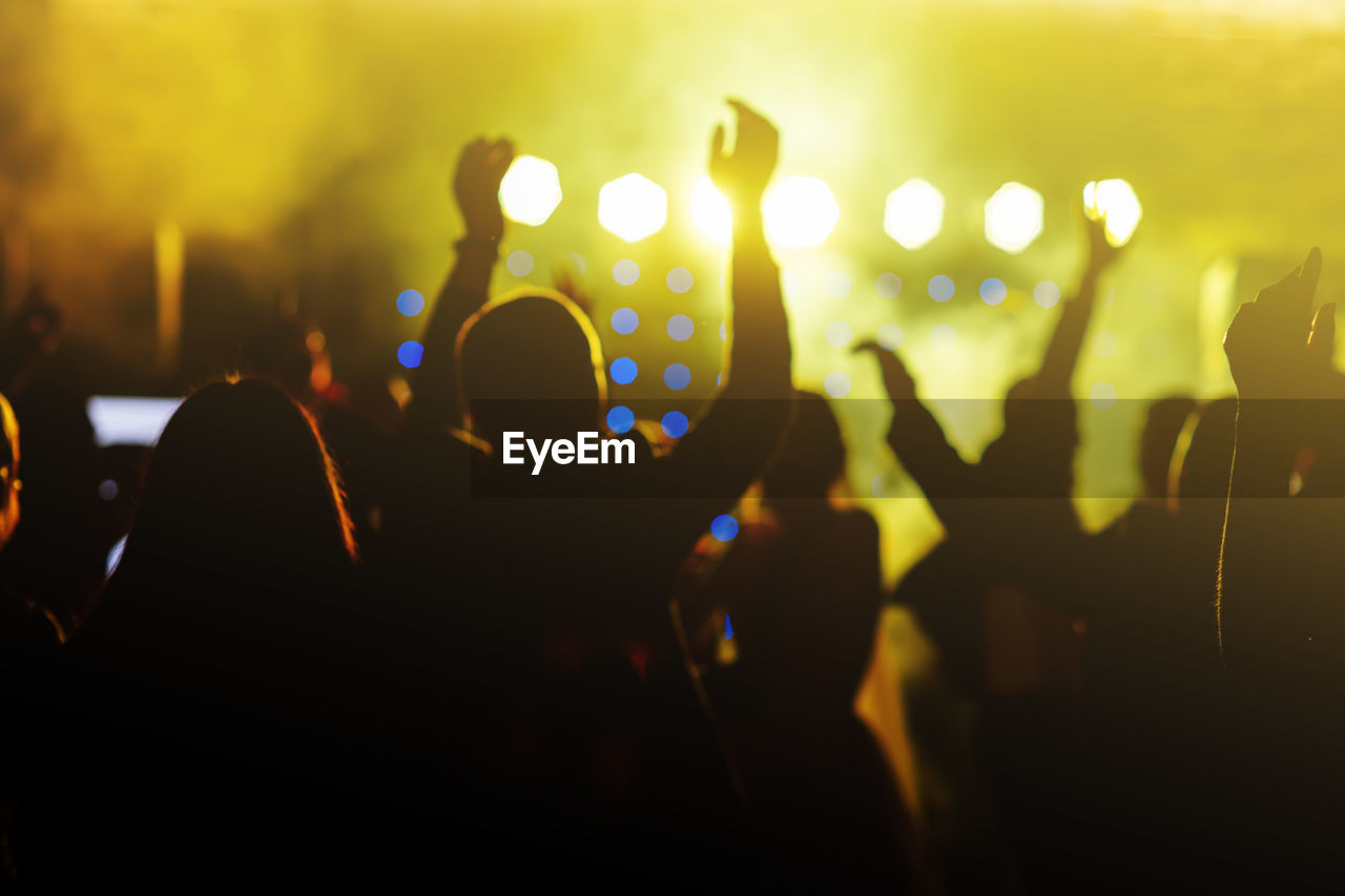 Cheering crowd in front of bright yellow stage lights. silhouette image of people dance in disco 