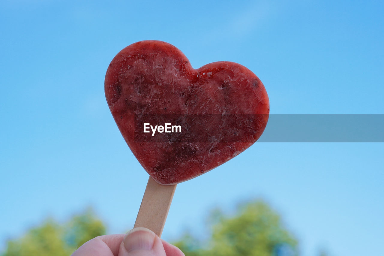 Hand holding heart shaped popsicle or ice lolly against clear blue sky - love summer concept