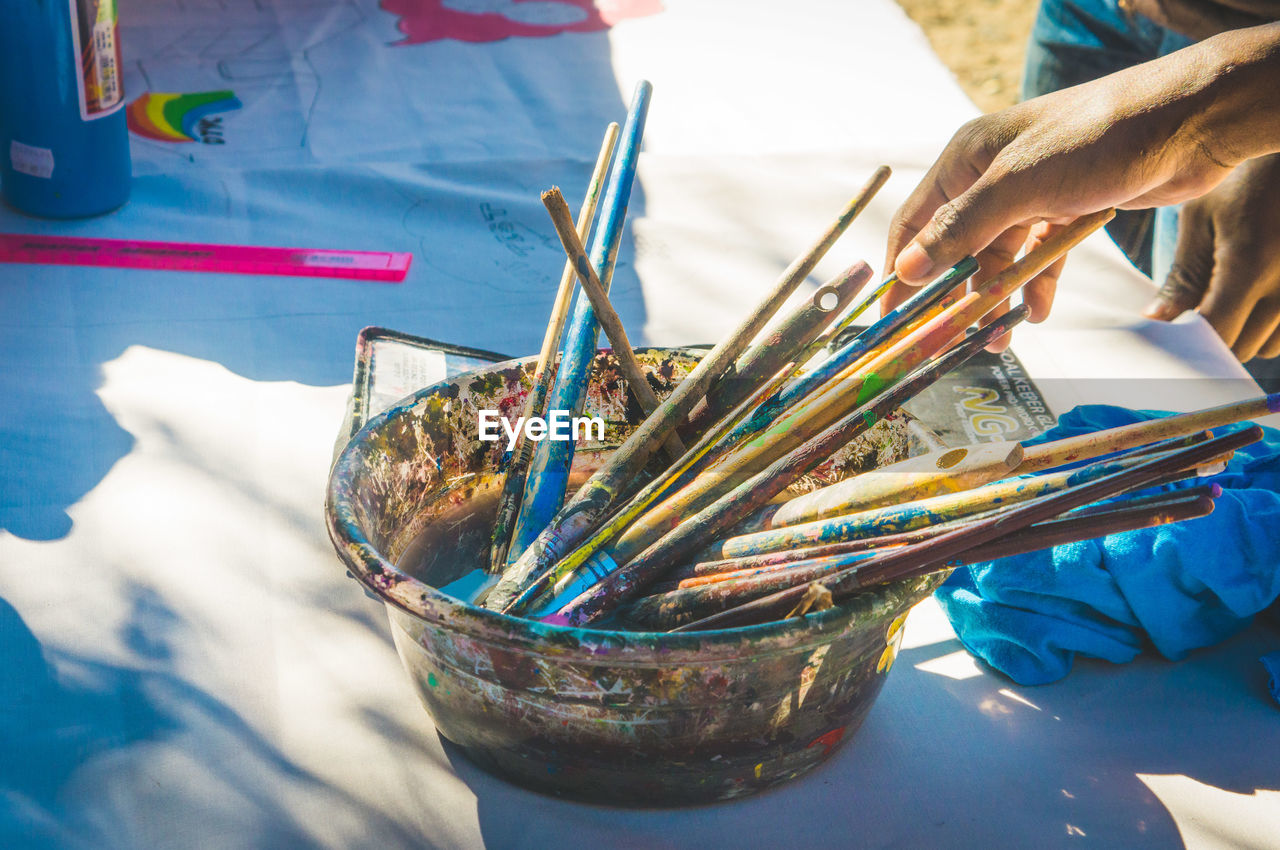 Cropped hand of painter reaching towards paintbrushes