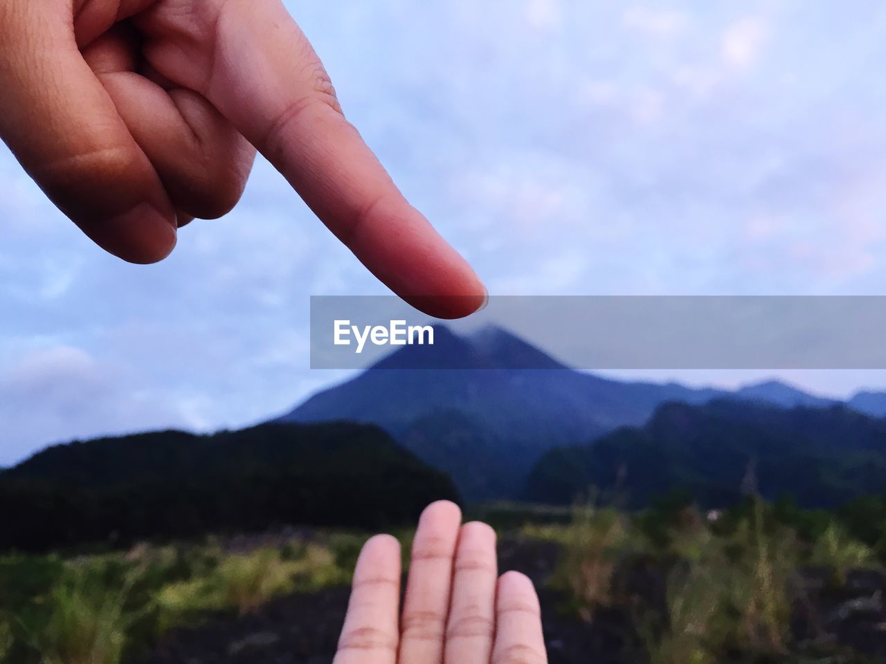 Close-up of hands gesturing over mountains against sky