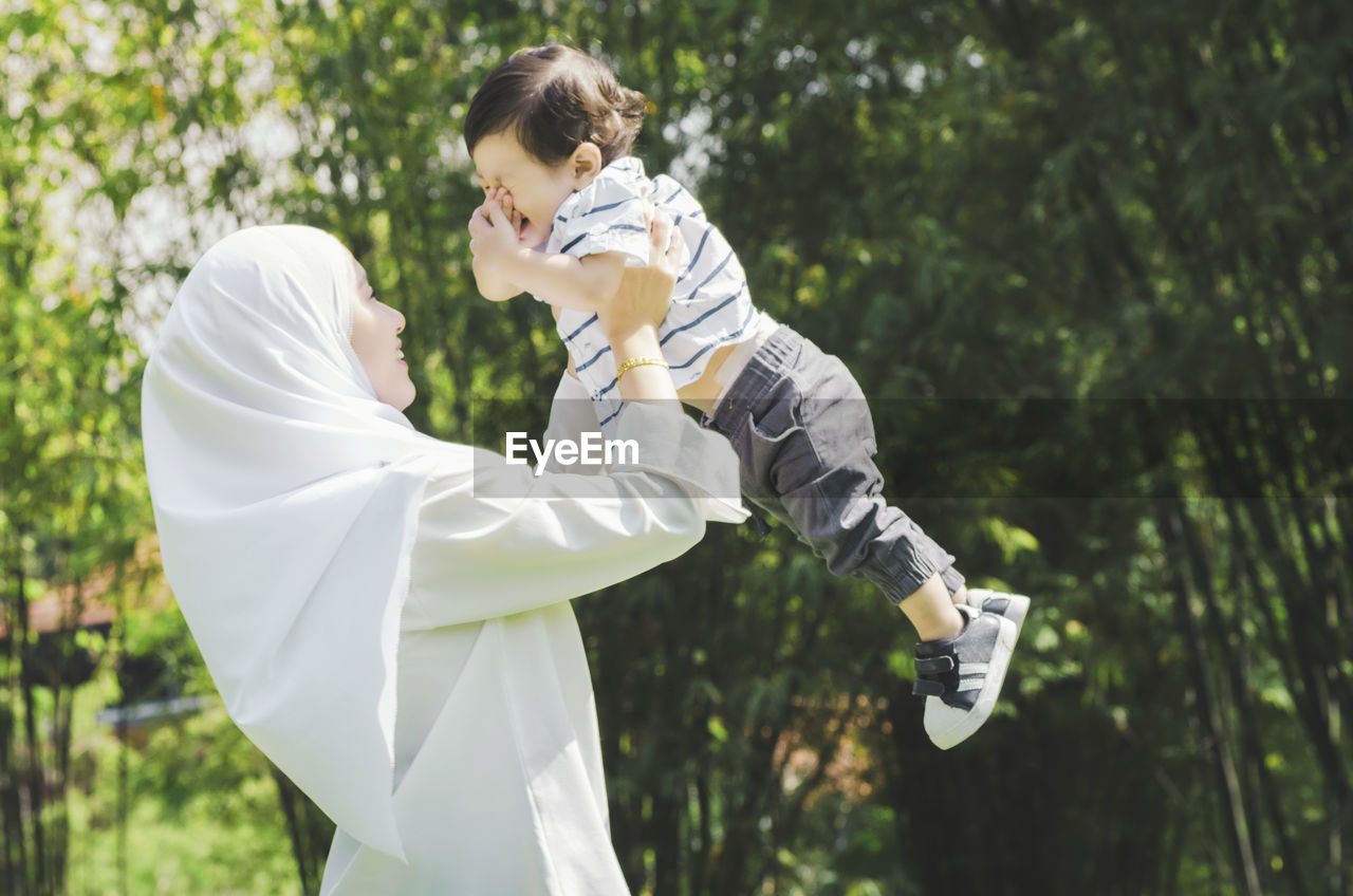 Side view of mother playing with son against trees