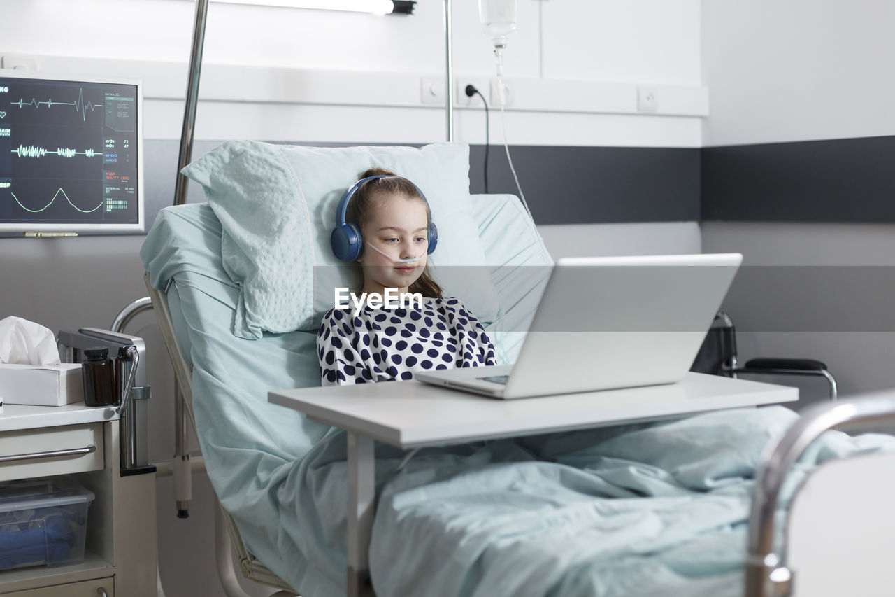Patients with oxygen tube looking at laptop in hospital