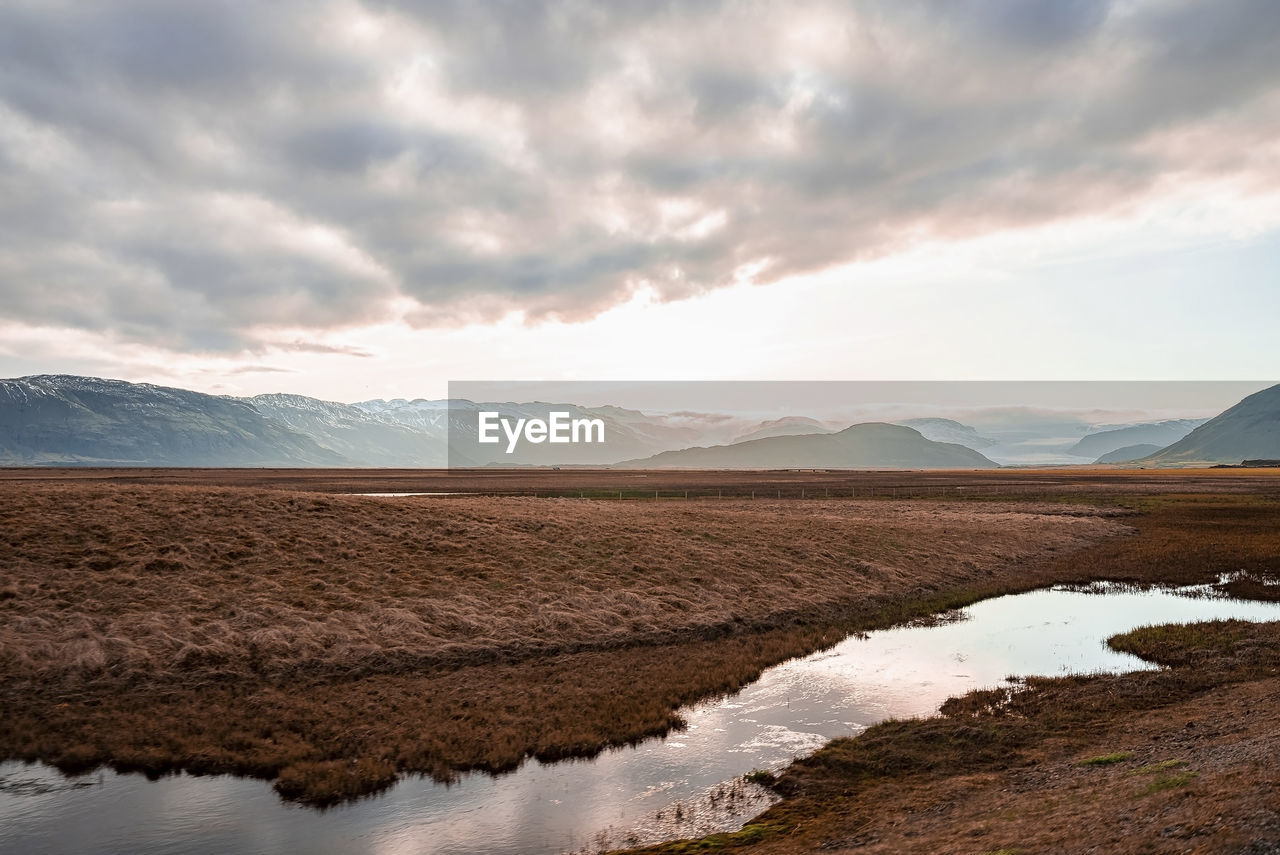 View of stream flowing amidst landscape in volcanic valley against cloudy sky